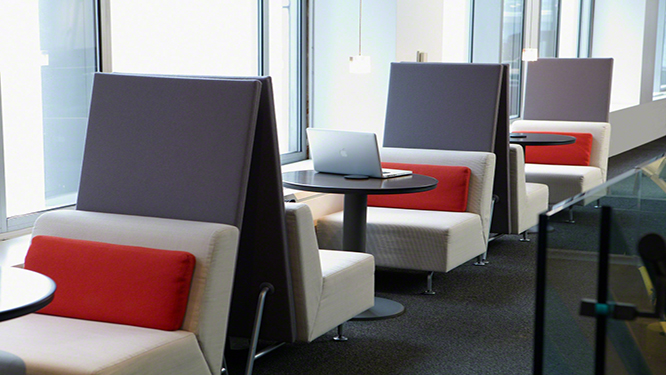 Cafe style single white lounge chairs with dark gray back dividers and red back cushions with small round black table in between them.