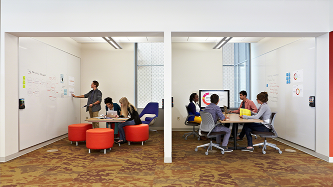 Two collaborative workspaces, one with a man standing at a large white board with two people sitting on orange stools and the other with a group of people sitting on conference chairs with a large monitor.