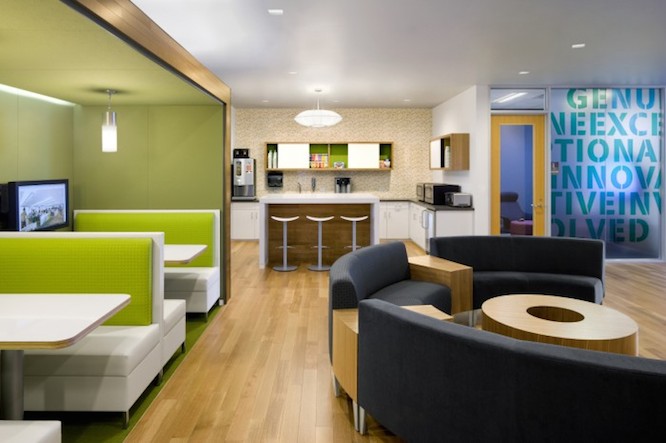 Cafe lounge area with green sofas, black rounded sofas, high top counter and kitchenette.