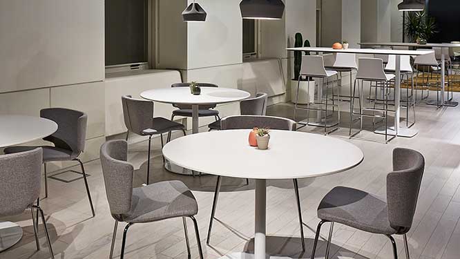 Open concept collaboration area with three round white tables with grey office chairs and high top white tables with white bar stools.