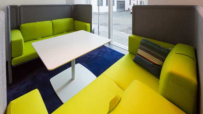 Lime green colored lounge sofas with dividers for privacy and large white table for collaboration.