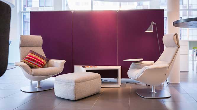 Rejuvenation space with grey lounge chairs and matching ottoman, white cube coffee table, grey floor lamp and purple wall divider.