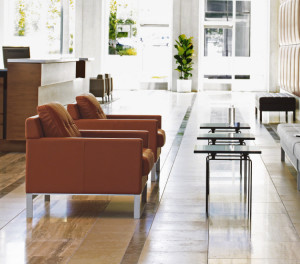 Grey office sofa, black side tables, and orange office lounge chairs in office waiting area