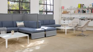 Two corner sectional couches, divided by high privacy screens, inside office lounge area with matching tables and chairs