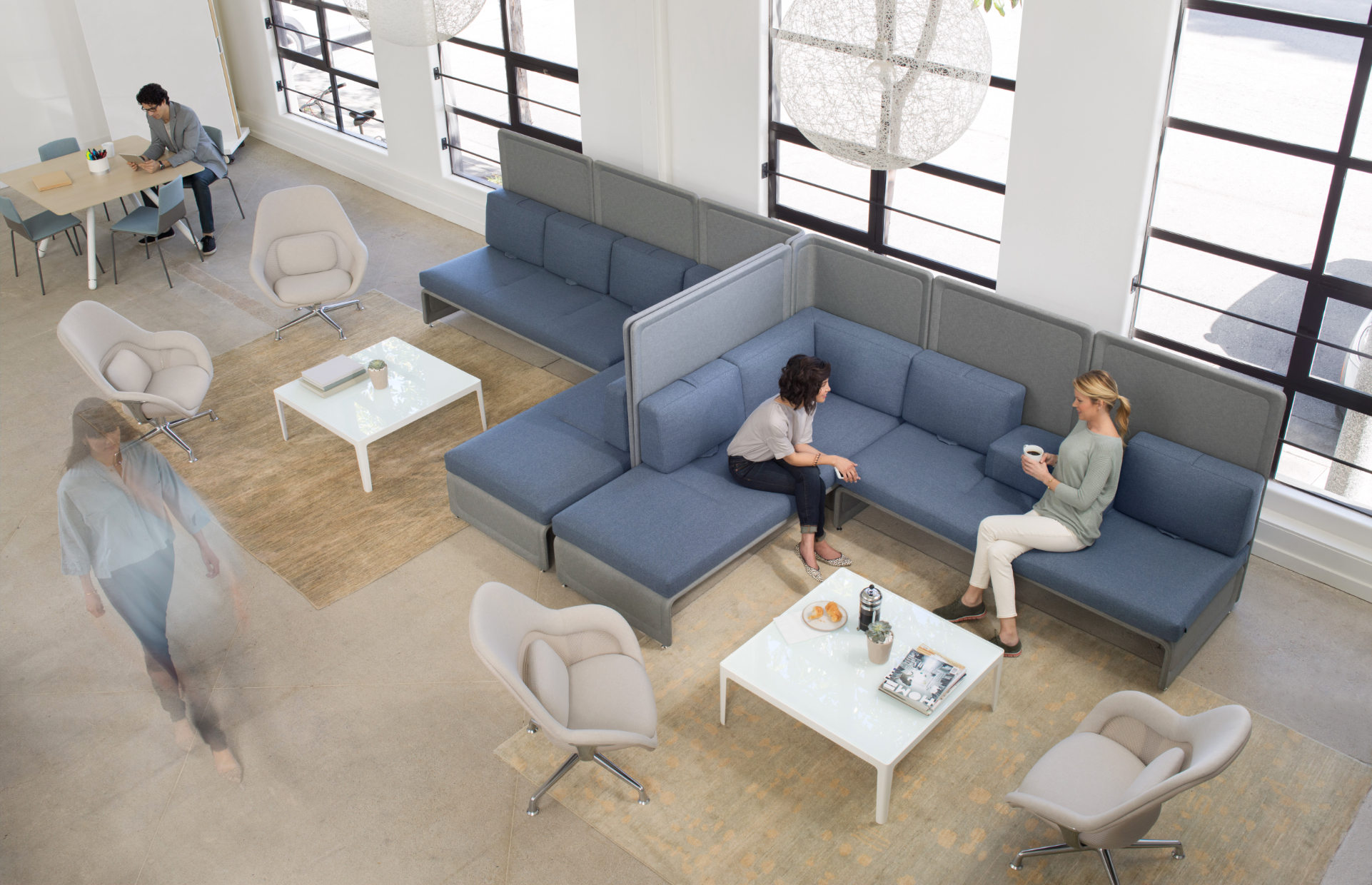 Space designed for social connection in office with blue sectional corner couches and high backed privacy screens surrounding white square coffee tables