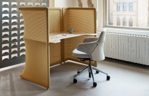 Brown mesh office space divider with attached work surface and grey mobile office chair