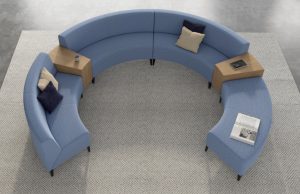 Round sectional couch on grey rug with wooden tables between couch segments