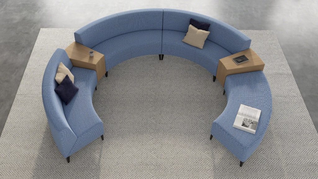 Round sectional couch on grey rug with wooden tables between couch segments
