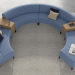 Round sectional couch on grey rug with wooden tables between couch segments