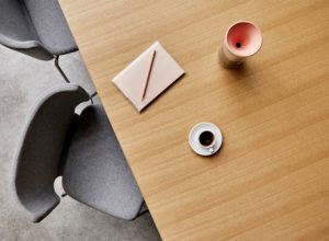 Wooden office conference table with grey upholstered chairs, notebook, and coffee cups