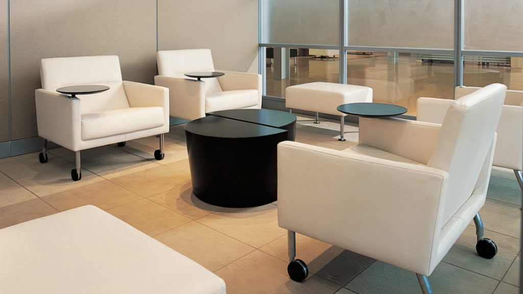 White armchairs with side tables and casters in office lounge area near small black coffee table