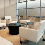 White armchairs with side tables and casters in office lounge area near small black coffee table