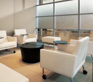 White armchairs with side tables and casters in office lounge area near small black coffee table
