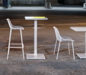 White outdoor tables, cafe-height tables, chairs and stools outside in a gas station parking lot