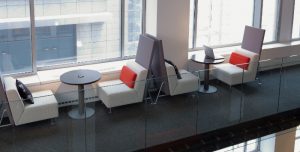 Office lounge bench seats with round tables and privacy screens in common area by windows