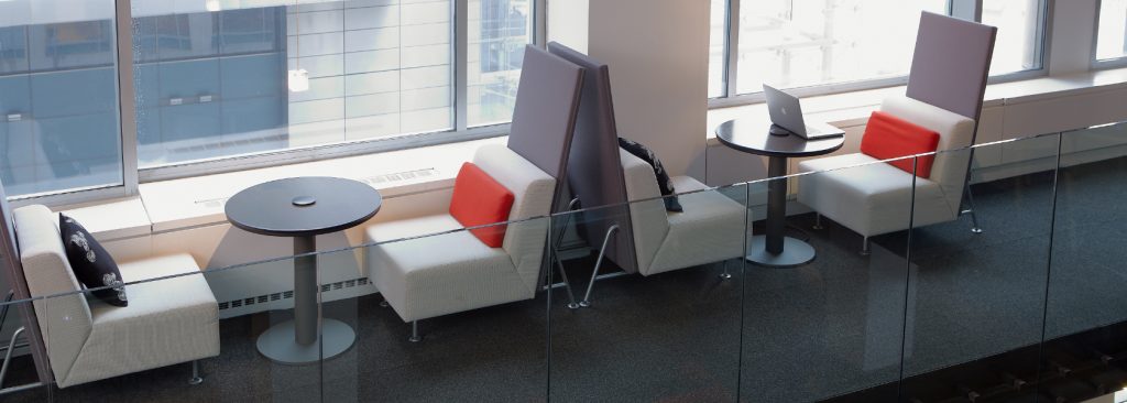 Office lounge bench seats with round tables and privacy screens in common area by windows