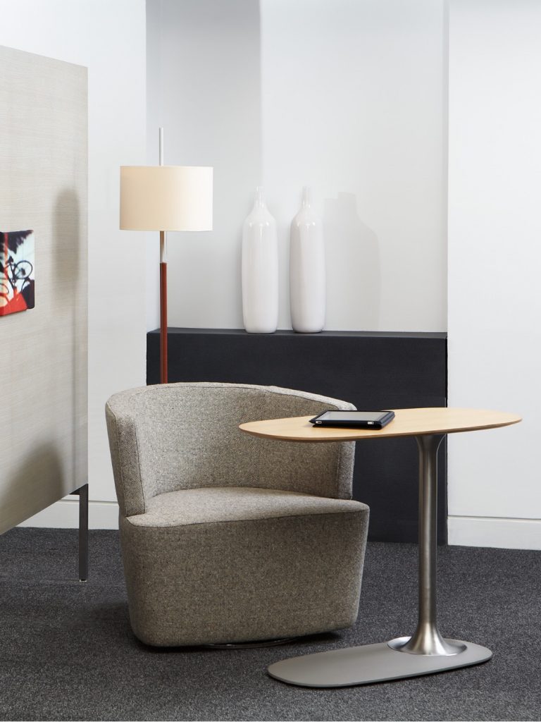 Grey round back office chair with side table, tall lamp, and wall decorations in lounge space