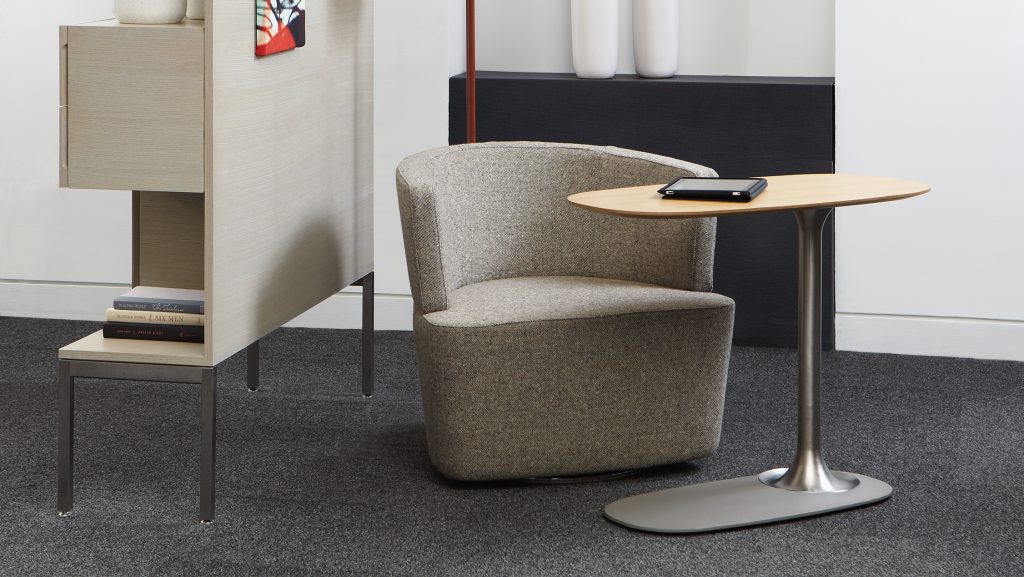 Grey round back office chair with side table, tall lamp, and wall decorations in lounge space