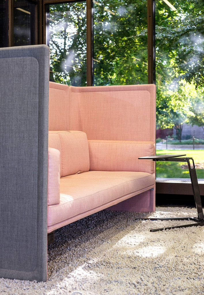 Pink and gray lounge seating with privacy screens and personal table placed next to a window in an office lounge setting.