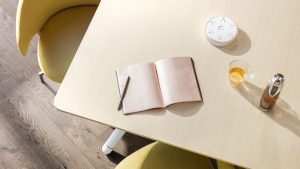 Wooden conference table with yellow seat, drinks, open journal, and desktop phone charging station