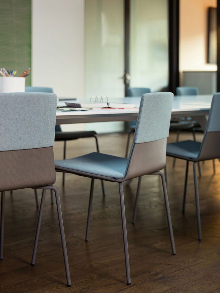 Wooden office side chairs with grey upholstery placed around a long conference room table