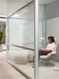 Woman reading magazine on high backed office chair in glass-walled office private space