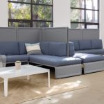 Two corner sectional couches, divided by high privacy screens, inside office lounge area with matching tables and chairs