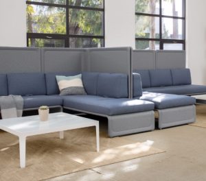 Two corner sectional couches, divided by high privacy screens, inside office lounge area with matching tables and chairs