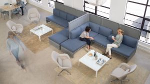 Space designed for social connection in office with blue sectional corner couches and high backed privacy screens surrounding white square coffee tables
