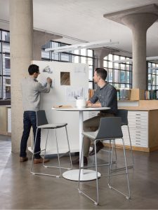 Two office workers collaborating on mobile whiteboard, seated at cafe-height table