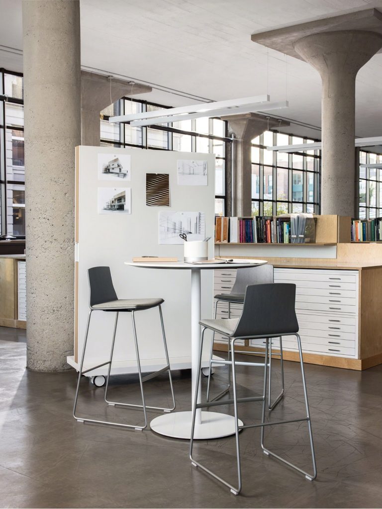 Collaborative space in office with tall table, side chairs, and mobile drywall holding photographs
