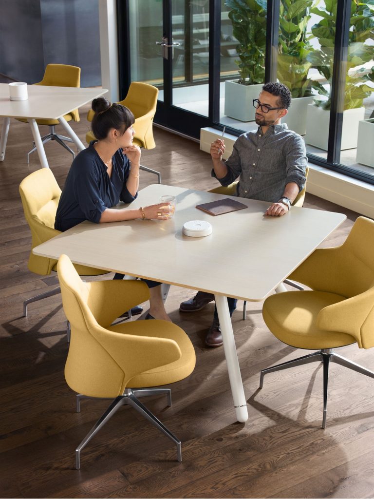 Two coworkers brainstorming around square office coffee table with yellow upholstered seating