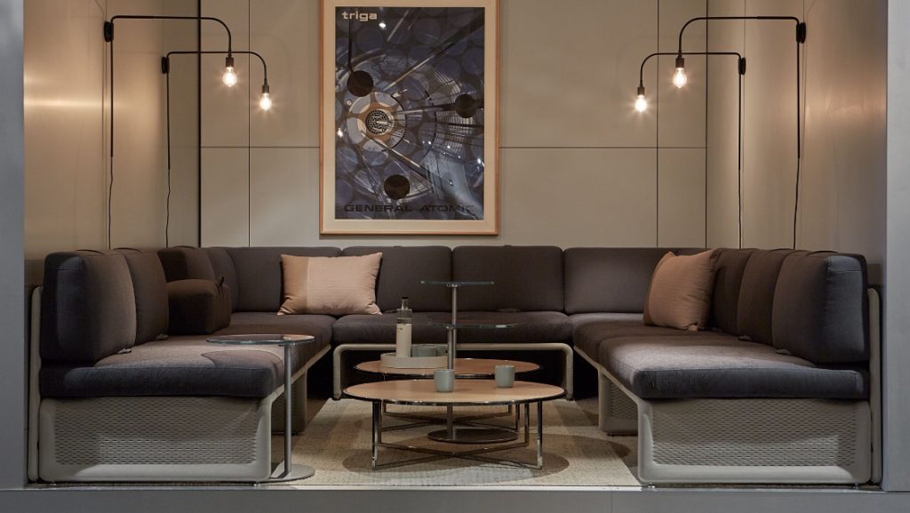 Recessed office social space with wall-to-wall sectional couch and two round circular coffee tables with metal frames
