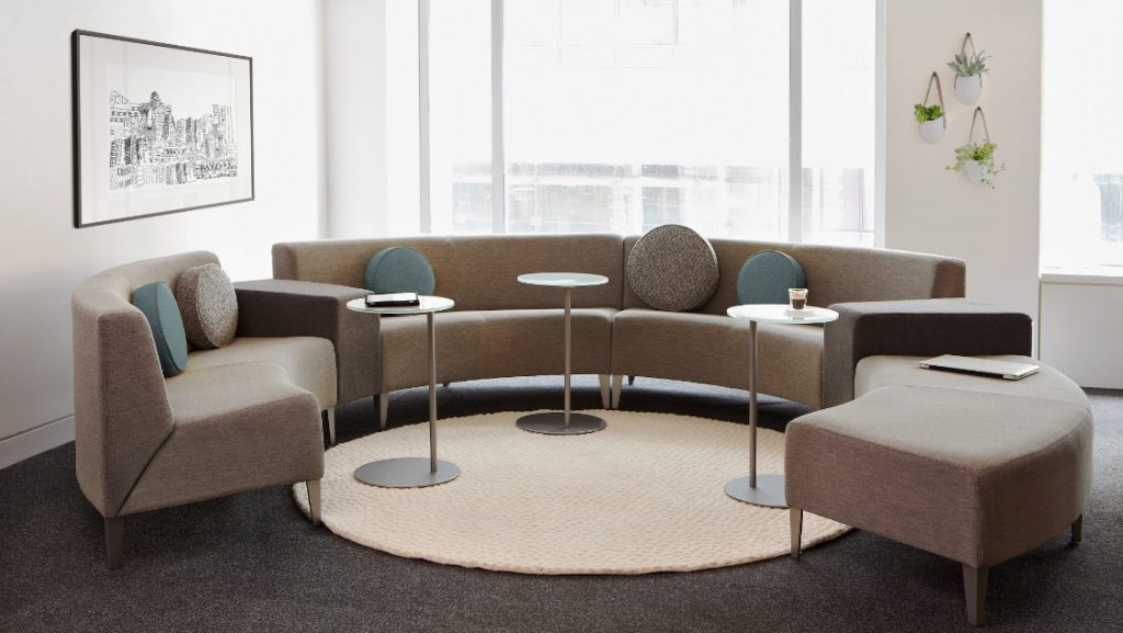 Circular grey office couch in corner of lounge space with side tables and matching bench seating