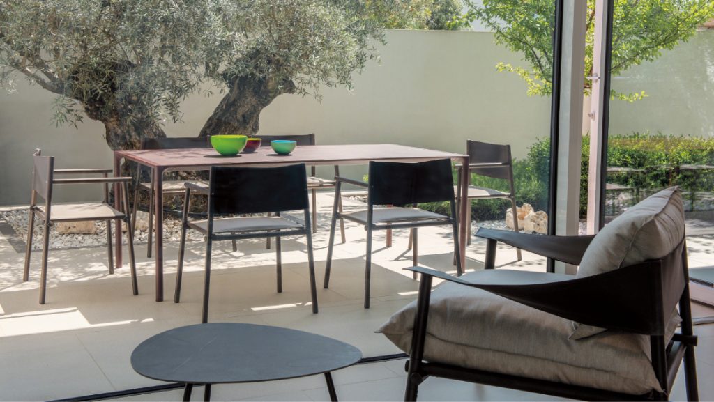 Outdoor pation lounge with chairs, long table for dining, and round side tables