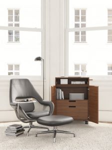 Quiet office focus area with black leather chair, matching ottoman, white side table, and dark wood open storage cabinet