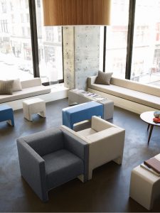 Office social space with long bench seating, matching stools and ottomans, armchairs, and round wooden side table