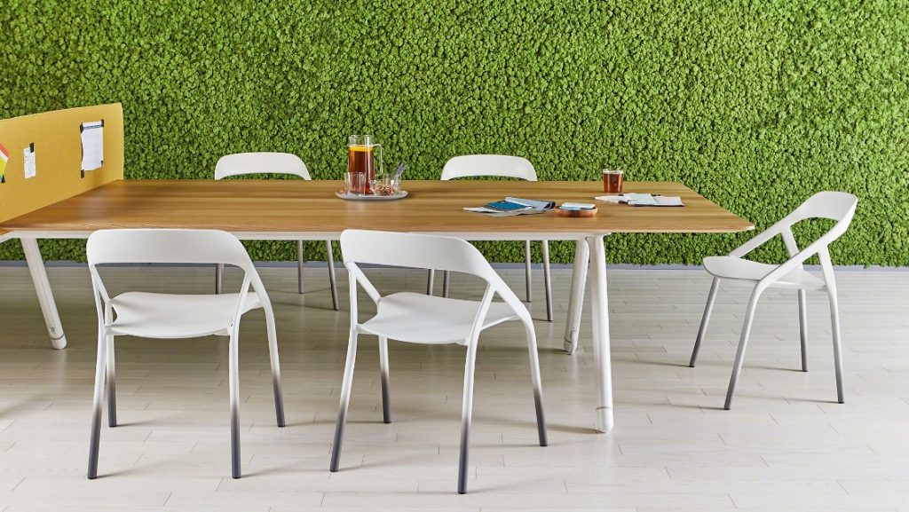 Outdoor office social space with ivy covered wall, wood-topped table, and outdoor dining chairs