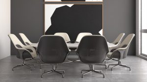 Modern office collaborative space with matching grey armchairs with black mesh back, white meeting room table, and art hanging on wall