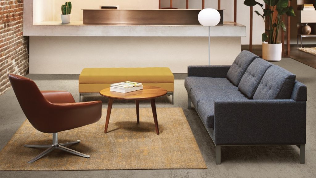 Small sitting area with brown leather lounge chair, charcoal sofa, yellow ottoman, small round wooden coffee table and brown rug