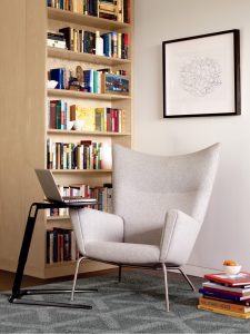 Office study area with wingback lounge chair, wooden bookcase, and side laptop table
