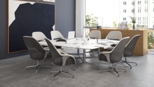 Grey upholstered high-back office chairs surrounding a white rectangular office table, with nearby wall art and wooden storage cabinets