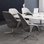 Grey upholstered high-back office chairs surrounding a white rectangular office table, with nearby wall art and wooden storage cabinets