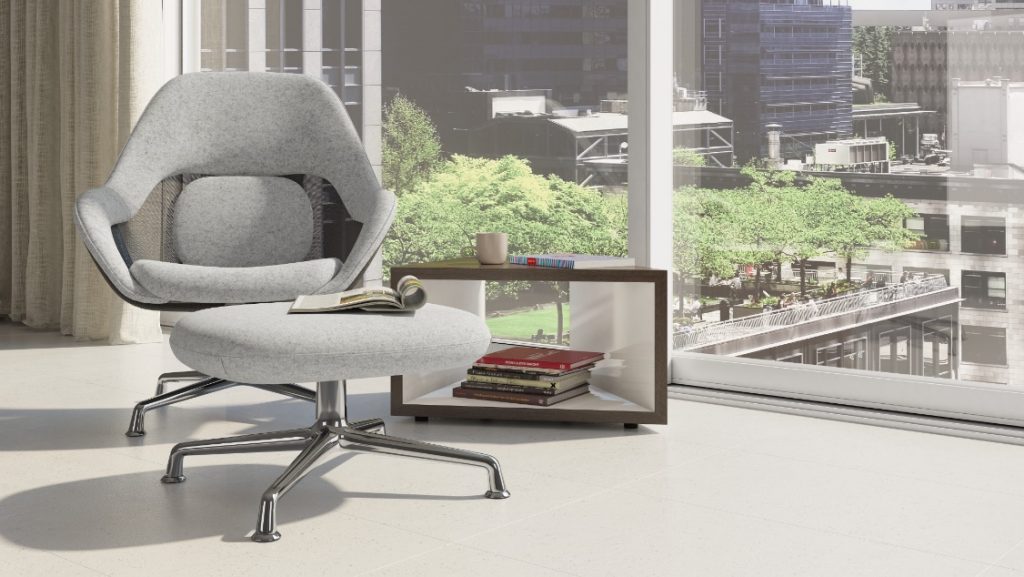 Quiet focus area in office with grey lounge chair, matching ottoman, and wooden bookcase with magazines