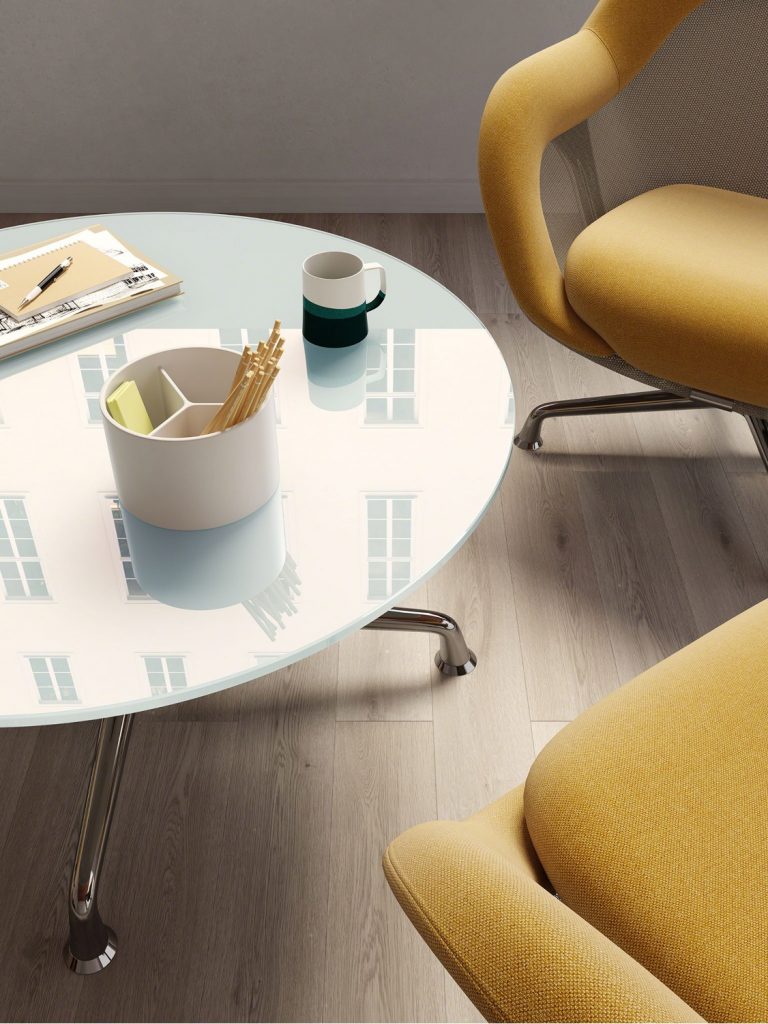 Corner social space in office with round glass coffee table and yellow upholstered lounge chairs