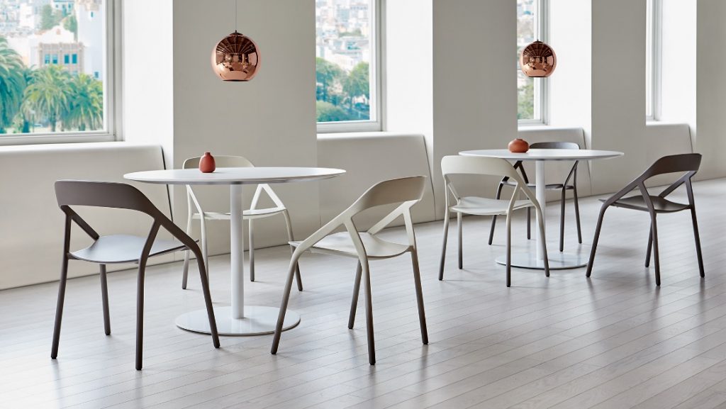 Office lounge area with round tables, slim chairs made of white and grey finished carbon fiber, and mirrored copper hanging lamps over each table