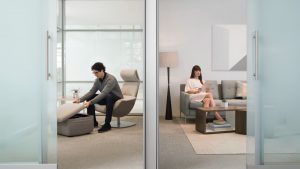 Two office workers using quiet rejuvenation space with high-backed chair, storage ottoman, and midcentury modern couch