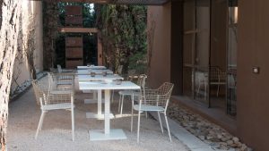 Rustic outdoor dining space with rock garden, white dining tables, and metal lattice outdoor chairs
