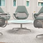 Office lounge space with green upholstered meeting chairs, round table in middle, and white outdoor rug