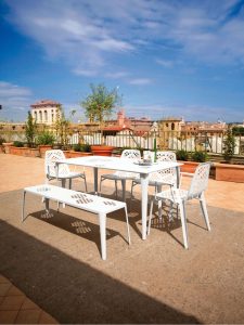 White outdoor table with matching bench and chairs on European rooftop overlooking a city skyline